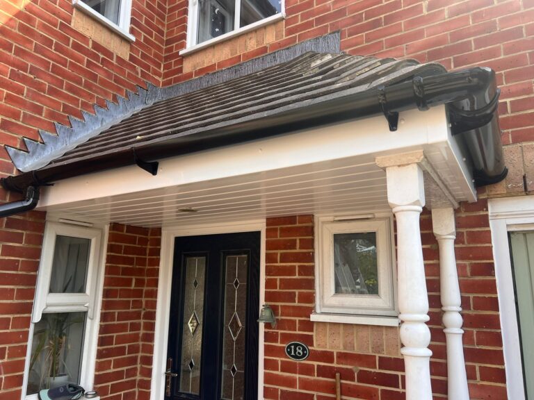 Close-up view of a home's front porch featuring white soffit boards, black guttering, and neatly installed white fascia under a tiled roof.