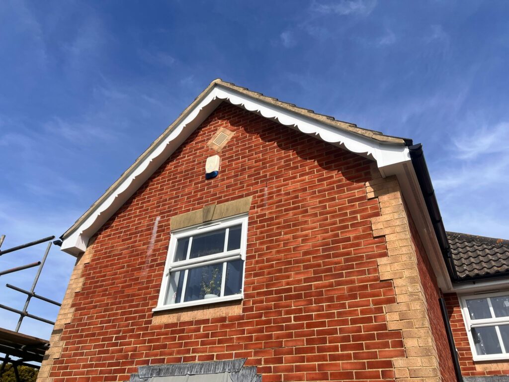 House exterior with decorative scalloped fascia trim along the gable, showing white uPVC detail against red brick.